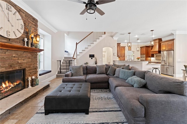 living area with arched walkways, crown molding, stairway, a large fireplace, and baseboards