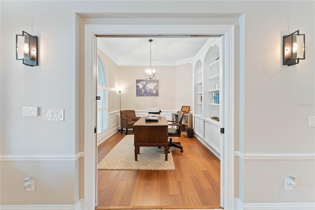 office featuring a chandelier, built in shelves, a wainscoted wall, ornamental molding, and light wood-type flooring