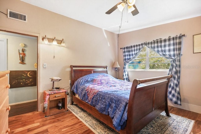 bedroom featuring baseboards, ceiling fan, visible vents, and wood finished floors