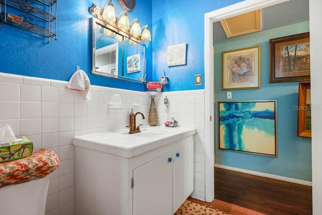 bathroom featuring tile walls, vanity, wood finished floors, wainscoting, and a textured wall