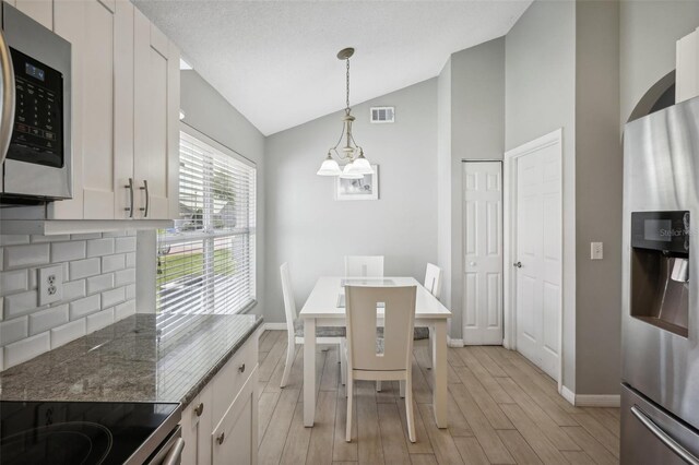 dining space featuring an inviting chandelier, lofted ceiling, light hardwood / wood-style floors, and a textured ceiling