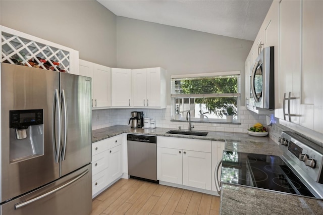 kitchen with lofted ceiling, appliances with stainless steel finishes, white cabinetry, and stone counters