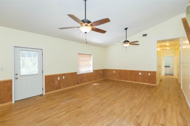 unfurnished room with ceiling fan, lofted ceiling, light wood-type flooring, and wood walls