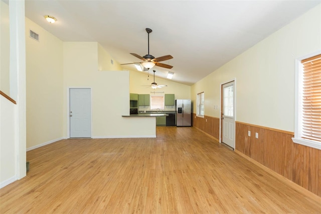 unfurnished living room featuring ceiling fan, lofted ceiling, wood walls, and light hardwood / wood-style floors