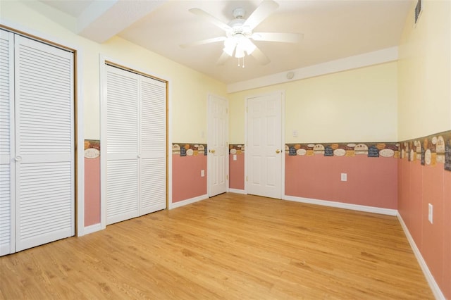 unfurnished bedroom featuring multiple closets, ceiling fan, and light hardwood / wood-style floors