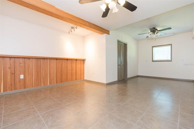 tiled empty room with ceiling fan, beamed ceiling, and wood walls