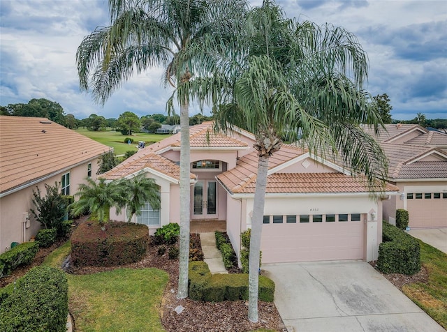 mediterranean / spanish house with french doors, an attached garage, a tile roof, and stucco siding