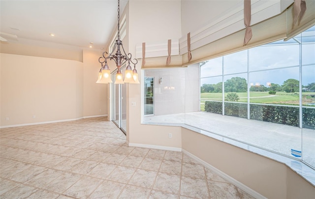 empty room featuring a wealth of natural light, a notable chandelier, a high ceiling, and baseboards