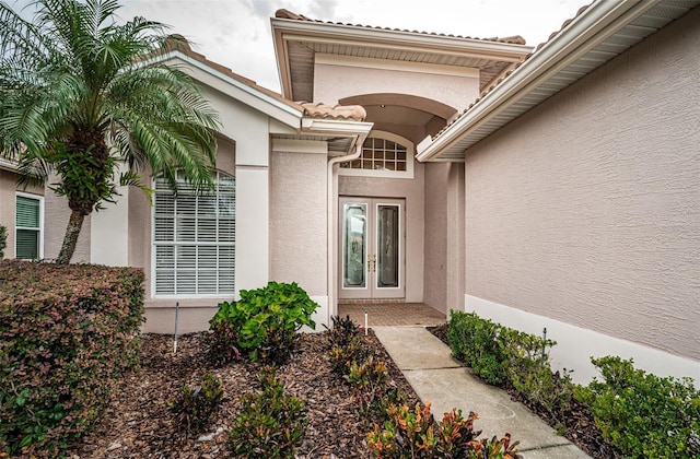 entrance to property featuring a tiled roof, french doors, and stucco siding