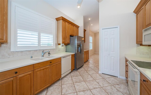 kitchen featuring a sink, decorative backsplash, white appliances, and plenty of natural light