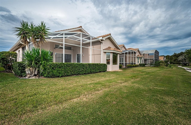 rear view of property with glass enclosure, a lawn, ceiling fan, and stucco siding