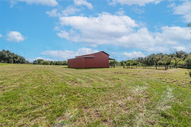 view of yard featuring an outdoor structure, fence, an outbuilding, and a rural view