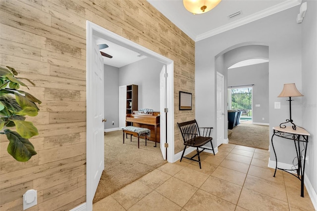 hallway featuring arched walkways, visible vents, baseboards, light colored carpet, and ornamental molding