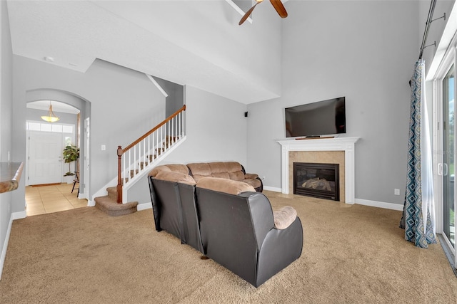 living area with stairway, a high ceiling, a ceiling fan, baseboards, and light colored carpet