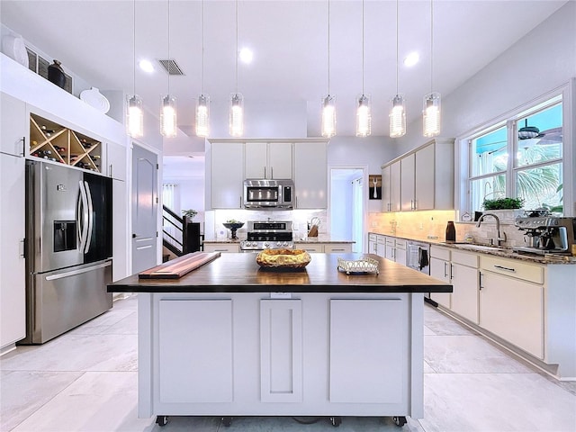 kitchen with appliances with stainless steel finishes, white cabinets, a center island, and decorative light fixtures