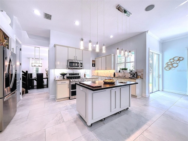 kitchen featuring pendant lighting, white cabinets, a kitchen island, backsplash, and appliances with stainless steel finishes