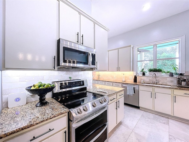 kitchen with stainless steel appliances, white cabinets, light stone counters, and sink