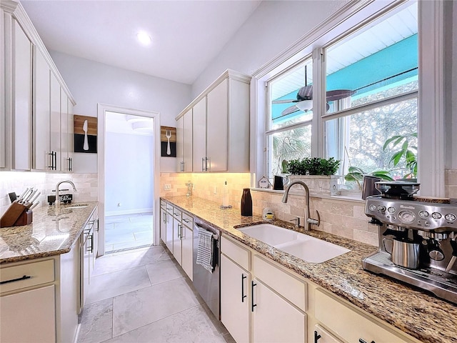 kitchen with light stone counters, stainless steel dishwasher, sink, and white cabinetry