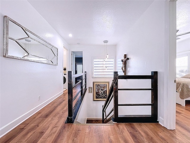 staircase with a notable chandelier, hardwood / wood-style floors, a textured ceiling, and washer / dryer