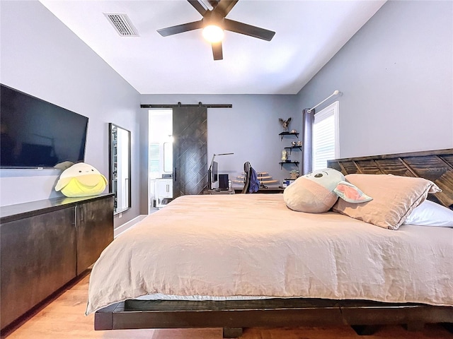 bedroom featuring ceiling fan, light wood-type flooring, a barn door, and lofted ceiling