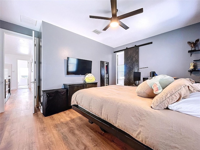 bedroom with a barn door, ceiling fan, multiple windows, and hardwood / wood-style flooring