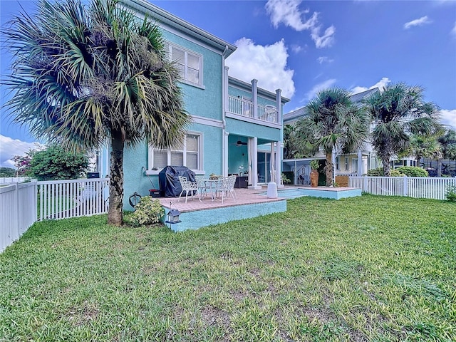 rear view of house with a lawn, a balcony, and a patio area