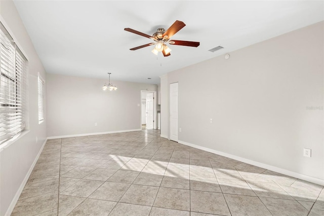 tiled spare room featuring ceiling fan with notable chandelier