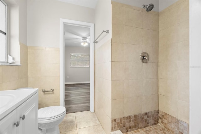 bathroom with tile patterned flooring, toilet, tiled shower, vanity, and tile walls