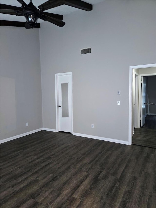 empty room with beam ceiling, a towering ceiling, ceiling fan, and dark hardwood / wood-style flooring