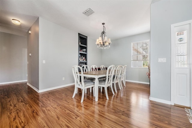 dining room with a notable chandelier, built in features, hardwood / wood-style floors, and a textured ceiling