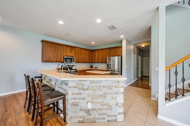 kitchen featuring a breakfast bar area, stainless steel appliances, a textured ceiling, light hardwood / wood-style flooring, and sink