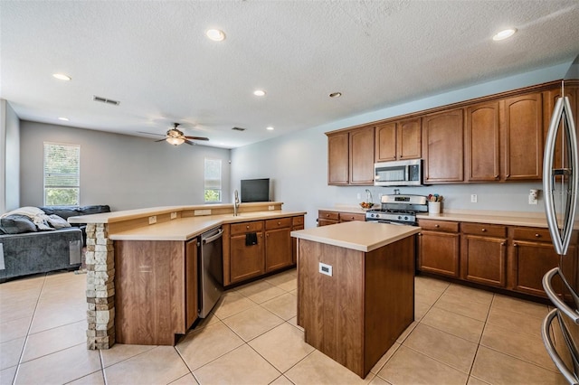 kitchen featuring light tile patterned flooring, a kitchen island, stainless steel appliances, a textured ceiling, and ceiling fan