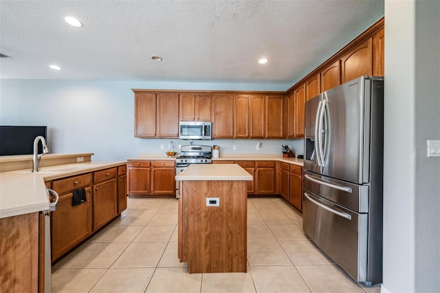 kitchen with appliances with stainless steel finishes, a textured ceiling, a center island, and light tile patterned floors