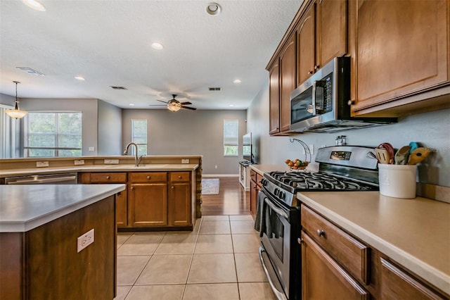 kitchen featuring appliances with stainless steel finishes, light tile patterned floors, ceiling fan, decorative light fixtures, and sink