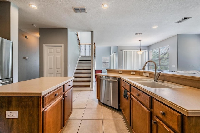 kitchen featuring an island with sink, appliances with stainless steel finishes, sink, and a textured ceiling