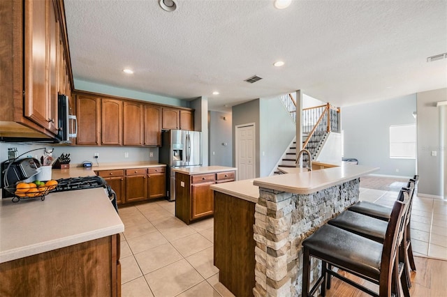 kitchen with an island with sink, stainless steel appliances, light tile patterned floors, and a breakfast bar