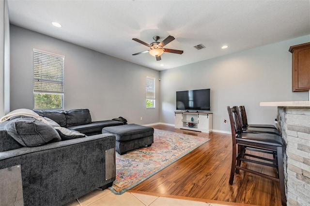 living room featuring light wood-type flooring, a stone fireplace, ceiling fan, and plenty of natural light