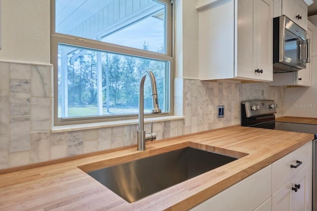 kitchen featuring sink, wooden counters, white cabinets, stainless steel appliances, and backsplash