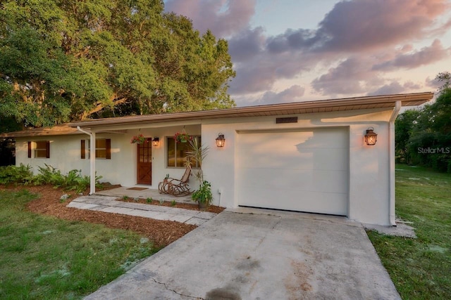 ranch-style house with a garage, covered porch, and a lawn