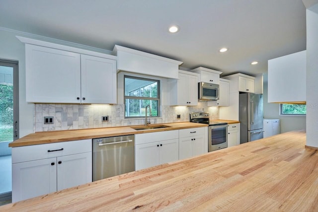 kitchen with a sink, stainless steel appliances, white cabinets, butcher block counters, and decorative backsplash