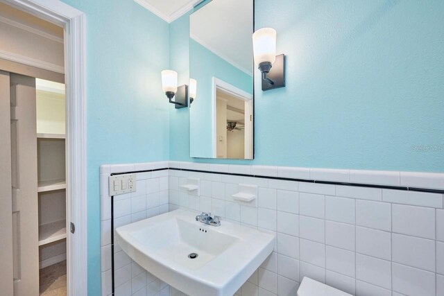 half bath with a sink, tile walls, wainscoting, and ornamental molding