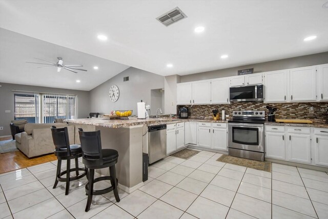 kitchen with a kitchen breakfast bar, stainless steel appliances, lofted ceiling, and white cabinetry