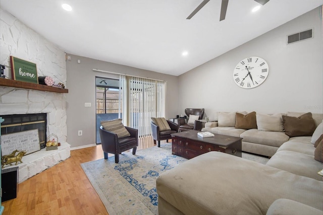 living room featuring light wood-type flooring, a fireplace, vaulted ceiling, and ceiling fan