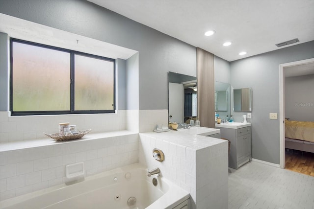 bathroom featuring tiled tub and vanity