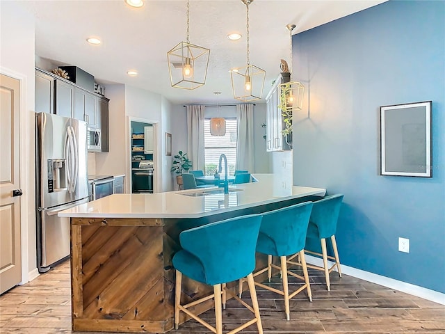 kitchen featuring sink, hanging light fixtures, light hardwood / wood-style floors, a breakfast bar, and appliances with stainless steel finishes