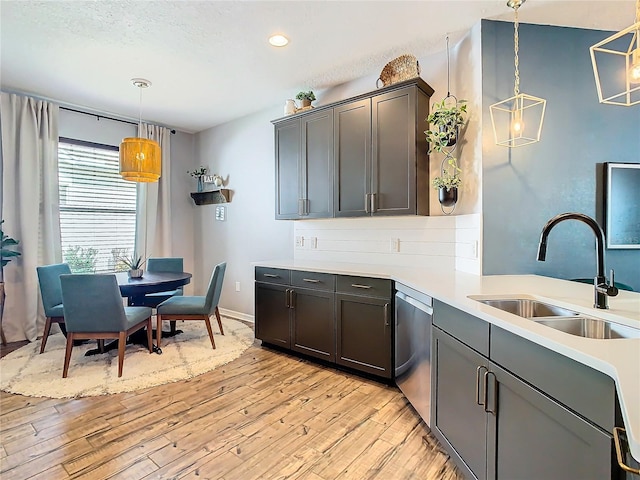 kitchen featuring sink, hanging light fixtures, light hardwood / wood-style flooring, stainless steel dishwasher, and a textured ceiling