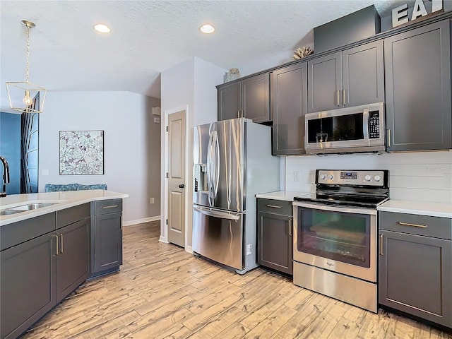 kitchen featuring sink, light hardwood / wood-style floors, pendant lighting, a textured ceiling, and appliances with stainless steel finishes