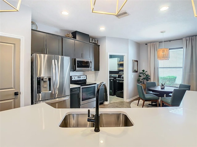 kitchen featuring washing machine and dryer, pendant lighting, stainless steel appliances, and sink