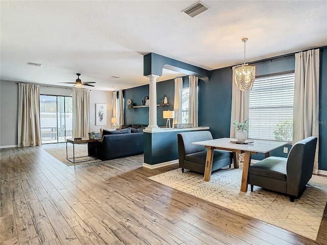 dining space featuring ornate columns, a wealth of natural light, light hardwood / wood-style floors, and ceiling fan with notable chandelier