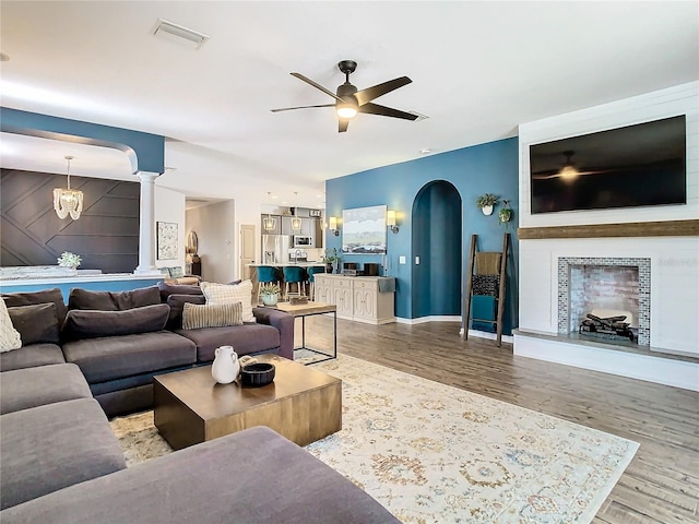 living room with ornate columns, wood-type flooring, and ceiling fan with notable chandelier